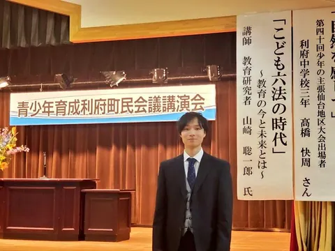 「こども六法の時代」の演題が掲げられた町民会議の講演会場に立つ山﨑聡一郎
