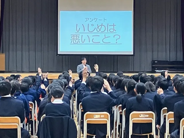 学校の体育館で「いじめは悪いこと？」と問いかけ、生徒たちが手を挙げて答えている様子